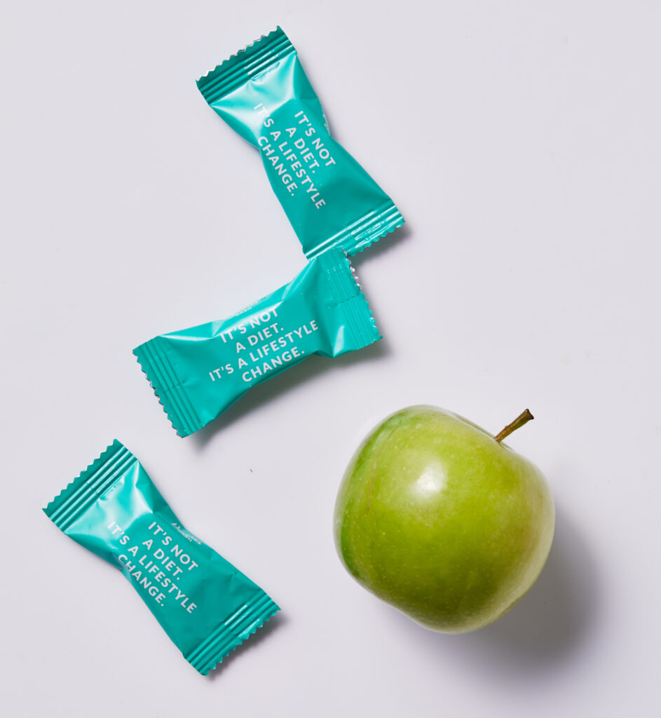 Three sachets of Vmores Dash probiotics supplement with a green apple 